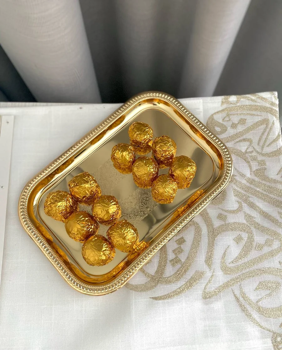 Gold-wrapped truffles on a gold tray over Arabic calligraphy linen
