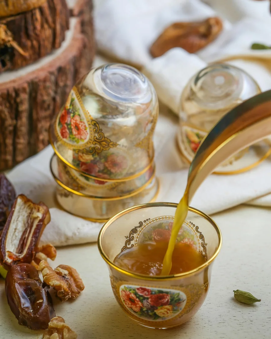 Omani coffee poured into a gold-rimmed cup, with dates and walnuts